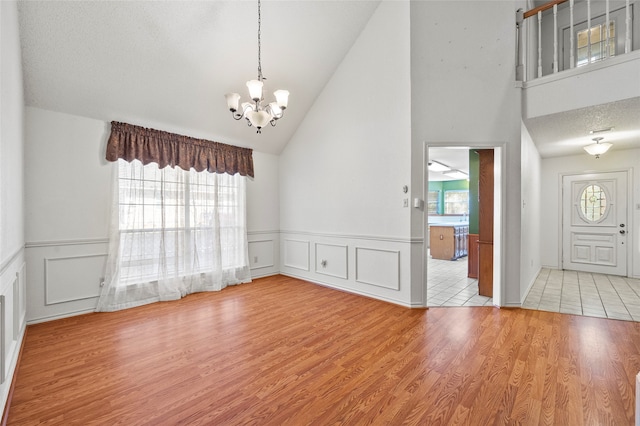 interior space with a textured ceiling, high vaulted ceiling, light tile patterned floors, and a notable chandelier