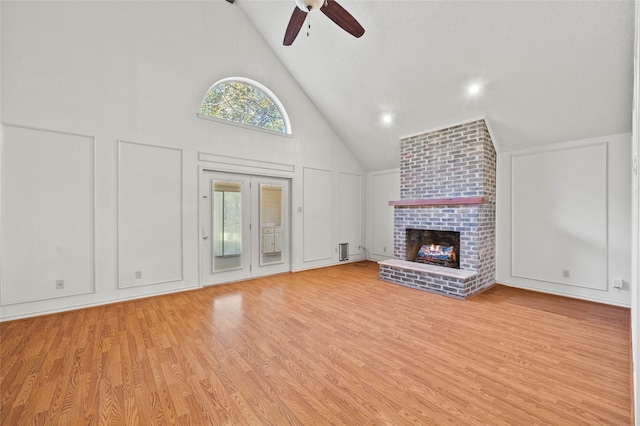 unfurnished living room featuring a brick fireplace, light wood-type flooring, high vaulted ceiling, and ceiling fan