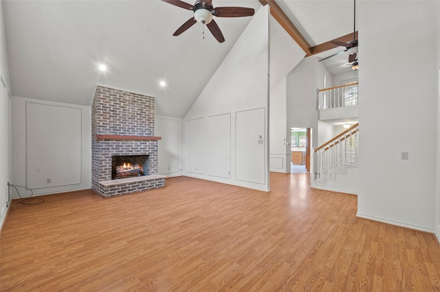 unfurnished living room featuring high vaulted ceiling, ceiling fan, beam ceiling, a fireplace, and light hardwood / wood-style floors