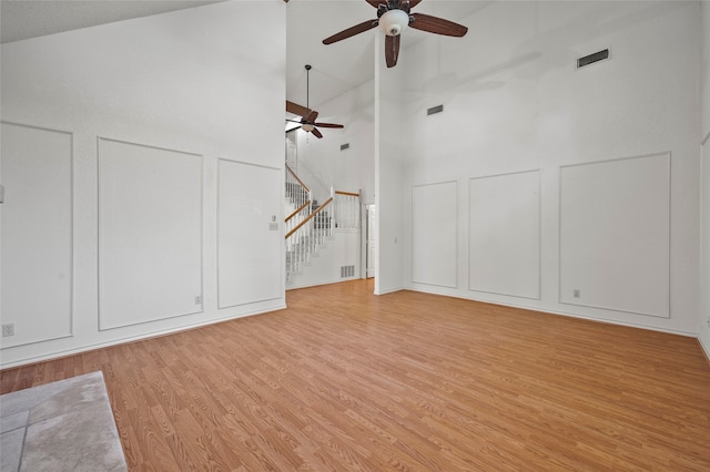 unfurnished living room with ceiling fan, light wood-type flooring, and high vaulted ceiling