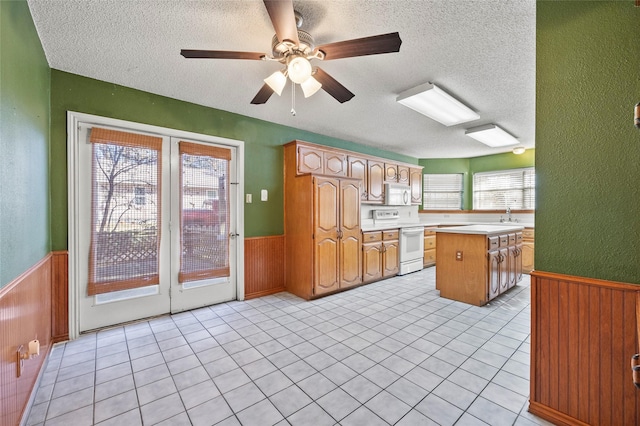 kitchen with a kitchen island, wooden walls, a textured ceiling, and white appliances