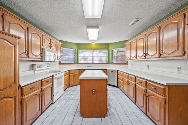 kitchen featuring sink, light tile patterned flooring, a textured ceiling, white appliances, and a kitchen island