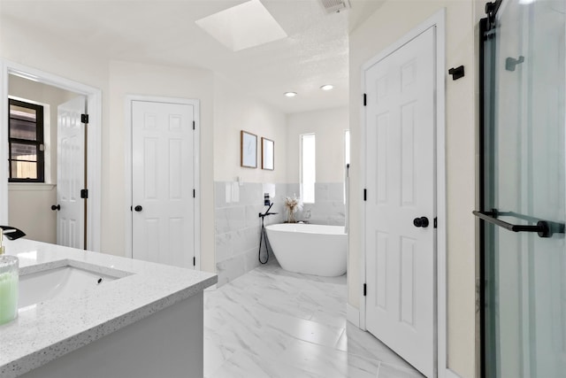 bathroom with vanity, shower with separate bathtub, tile walls, and a skylight