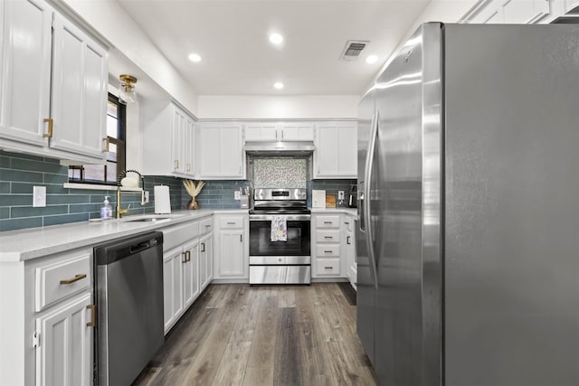 kitchen with dark wood-type flooring, sink, stainless steel appliances, range hood, and white cabinets