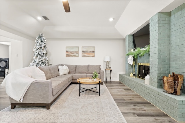 living room with a fireplace, washer / dryer, light hardwood / wood-style floors, and lofted ceiling