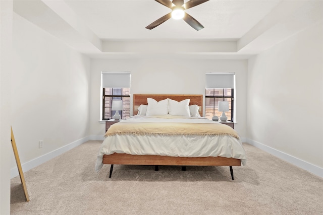 carpeted bedroom with a raised ceiling and ceiling fan