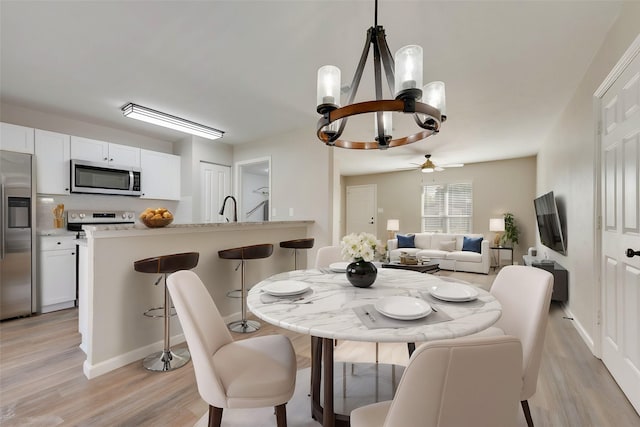 dining area featuring sink, ceiling fan with notable chandelier, and light wood-type flooring