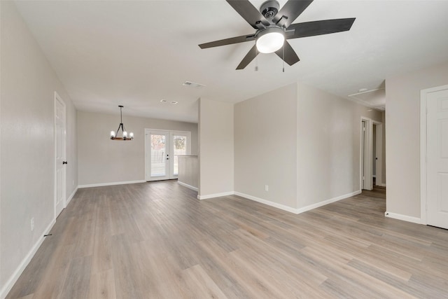 empty room with french doors, ceiling fan with notable chandelier, and light hardwood / wood-style floors