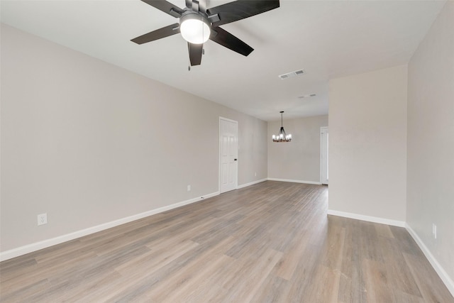 empty room with ceiling fan with notable chandelier and light hardwood / wood-style flooring