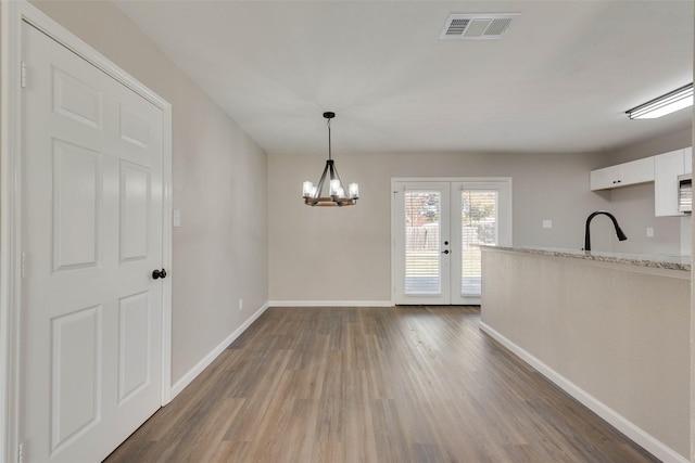 unfurnished dining area with a chandelier, french doors, dark wood-type flooring, and sink