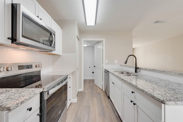 kitchen with sink, tasteful backsplash, light stone counters, white cabinetry, and stainless steel appliances