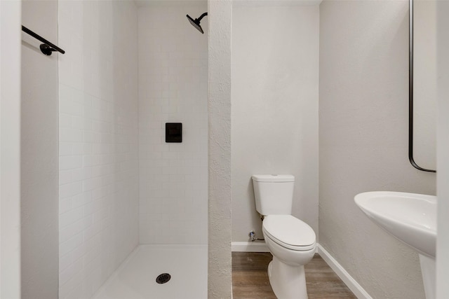 bathroom with a tile shower, wood-type flooring, and toilet