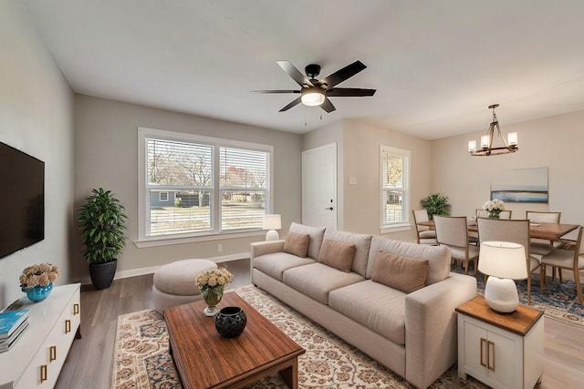 living room featuring ceiling fan with notable chandelier and light wood-type flooring