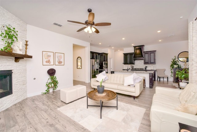 living room with a fireplace, ceiling fan, and light wood-type flooring