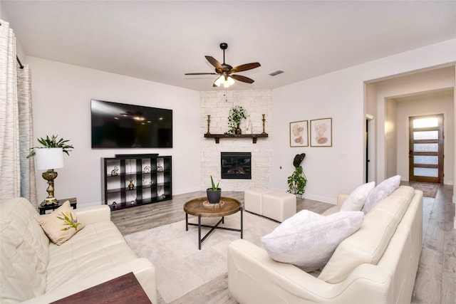 living room featuring ceiling fan, a stone fireplace, and light hardwood / wood-style floors