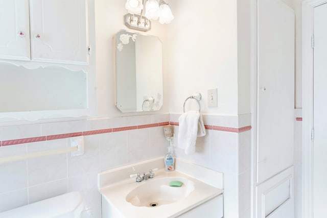 bathroom with a wainscoted wall, vanity, toilet, and tile walls