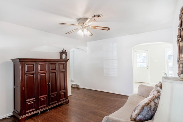 living area with dark wood-type flooring, arched walkways, visible vents, and a ceiling fan