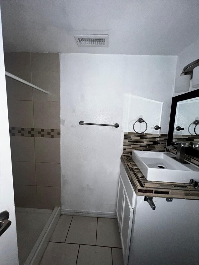 bathroom with tile patterned flooring, a tile shower, and sink