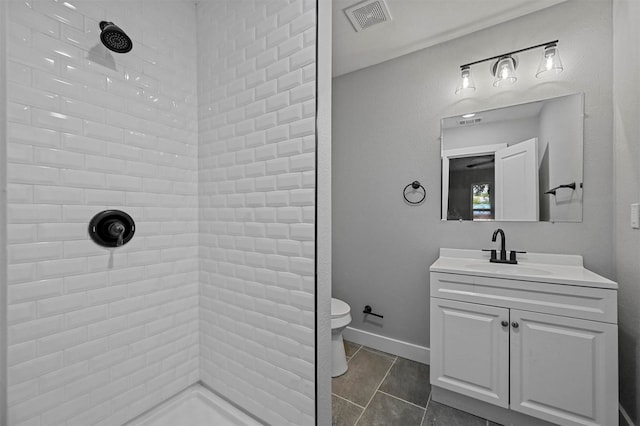 bathroom with tile patterned flooring, vanity, a tile shower, and toilet