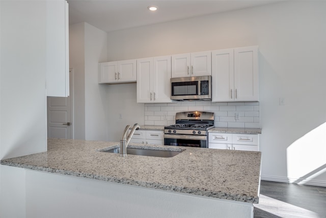 kitchen with white cabinets, sink, light stone countertops, kitchen peninsula, and stainless steel appliances