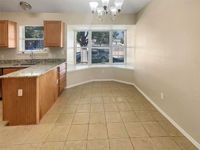 kitchen featuring a notable chandelier, a healthy amount of sunlight, light stone counters, and sink