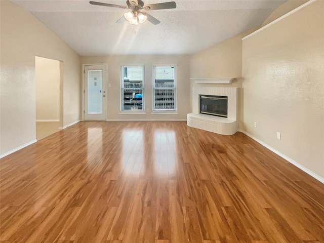 unfurnished living room featuring vaulted ceiling, hardwood / wood-style flooring, ceiling fan, a textured ceiling, and a tiled fireplace