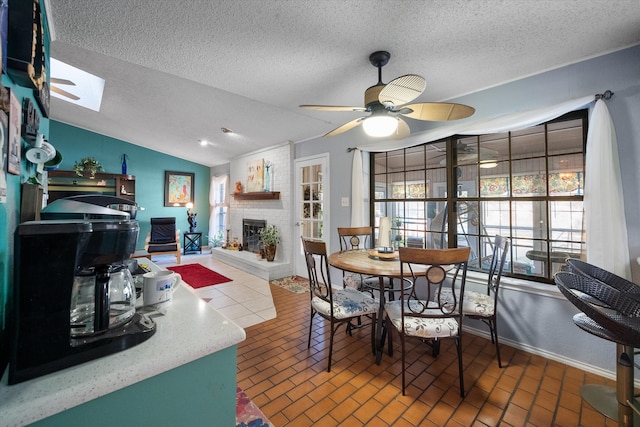 dining space with a textured ceiling, ceiling fan, lofted ceiling with skylight, and a fireplace