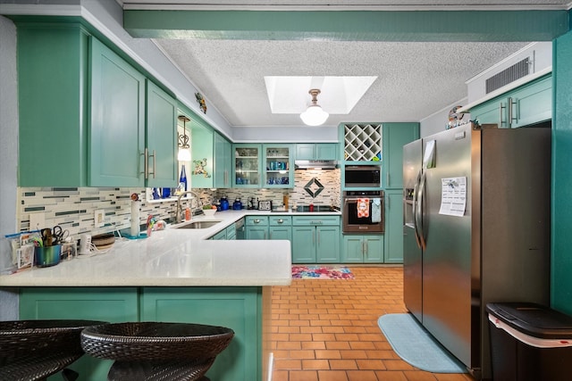 kitchen with kitchen peninsula, decorative backsplash, a skylight, stainless steel appliances, and sink