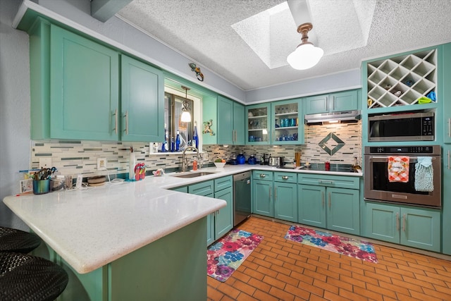 kitchen featuring a skylight, decorative light fixtures, sink, kitchen peninsula, and stainless steel appliances