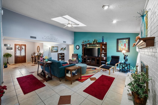 tiled living room with vaulted ceiling with skylight, ceiling fan, a textured ceiling, and a brick fireplace