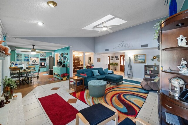 tiled living room featuring vaulted ceiling with skylight, ceiling fan, and a textured ceiling