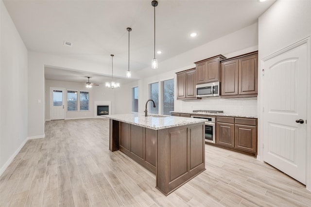 kitchen featuring pendant lighting, stainless steel appliances, light stone countertops, a center island with sink, and light hardwood / wood-style flooring