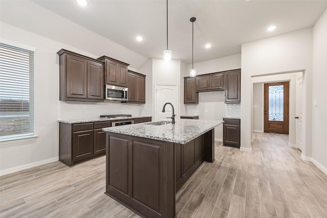 kitchen featuring sink, hanging light fixtures, light stone counters, stainless steel appliances, and a center island with sink