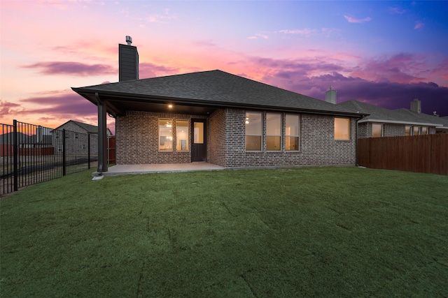 back house at dusk with a yard and a patio