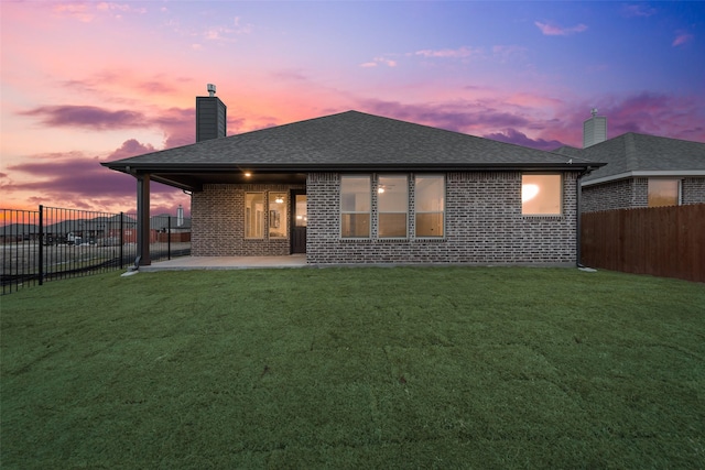 back house at dusk featuring a patio and a lawn