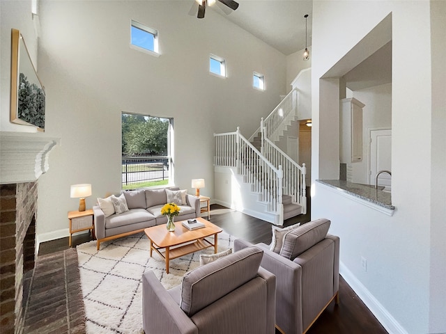 living room with ceiling fan, a towering ceiling, wood-type flooring, and a brick fireplace