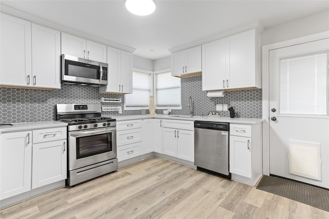 kitchen with sink, white cabinetry, tasteful backsplash, appliances with stainless steel finishes, and light hardwood / wood-style floors