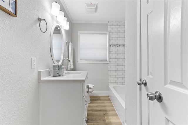 full bathroom with tiled shower / bath, hardwood / wood-style flooring, vanity, toilet, and crown molding