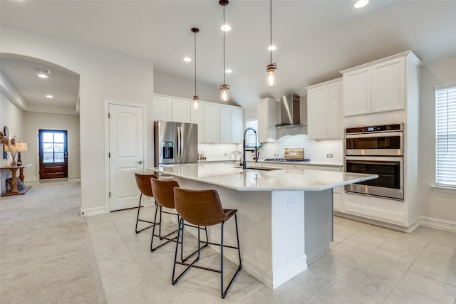 kitchen featuring sink, appliances with stainless steel finishes, a kitchen island with sink, hanging light fixtures, and wall chimney exhaust hood