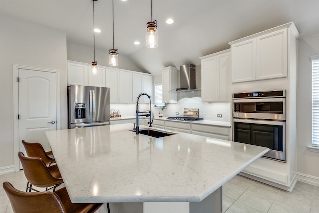 kitchen with sink, wall chimney exhaust hood, hanging light fixtures, a center island with sink, and appliances with stainless steel finishes