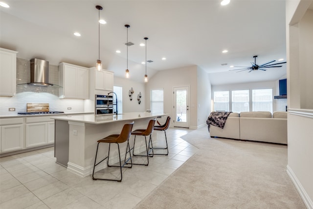 kitchen with pendant lighting, lofted ceiling, a center island with sink, white cabinets, and wall chimney exhaust hood