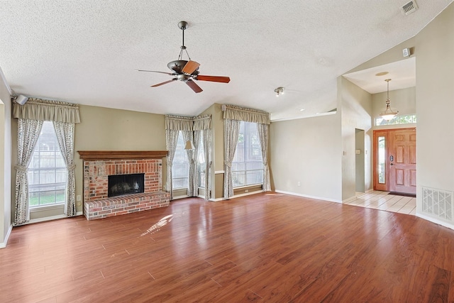 unfurnished living room with lofted ceiling, a brick fireplace, and light hardwood / wood-style flooring