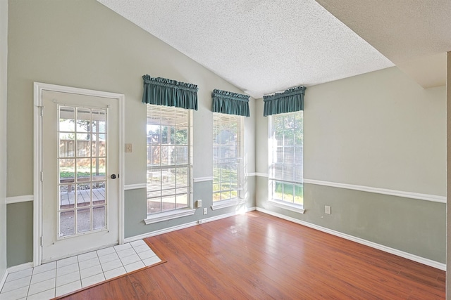 empty room with wood-type flooring, lofted ceiling, and a textured ceiling