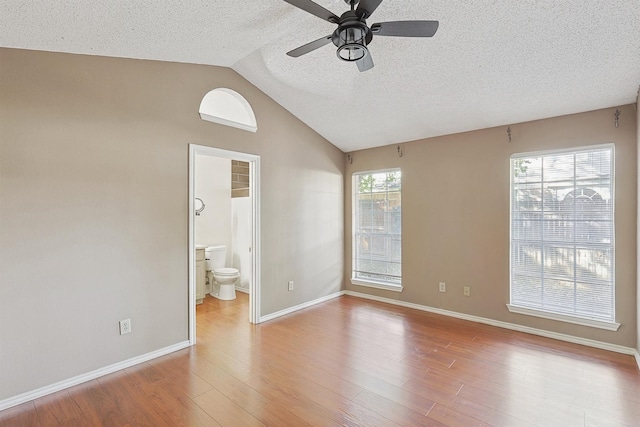 unfurnished bedroom featuring lofted ceiling, ensuite bathroom, light hardwood / wood-style flooring, and a textured ceiling