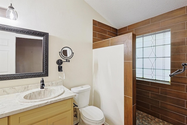 bathroom featuring tiled shower, toilet, vaulted ceiling, a textured ceiling, and vanity