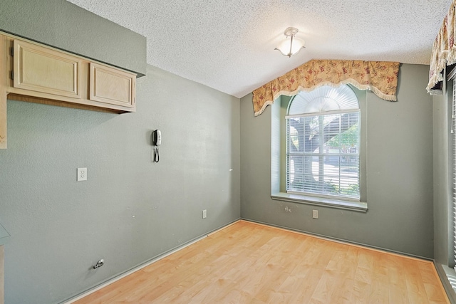 unfurnished dining area featuring lofted ceiling, a textured ceiling, and light wood-type flooring