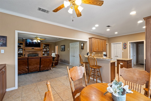 dining space featuring ceiling fan, crown molding, a textured ceiling, a fireplace, and light tile patterned floors