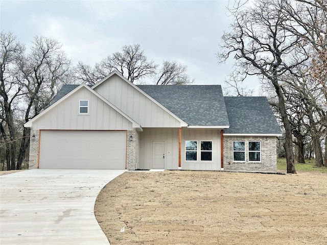 view of front facade featuring brick siding, a shingled roof, an attached garage, board and batten siding, and driveway