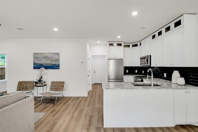 kitchen with backsplash, white cabinets, light wood-type flooring, light stone countertops, and appliances with stainless steel finishes