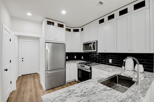 kitchen featuring light wood-type flooring, tasteful backsplash, light stone counters, white cabinetry, and stainless steel appliances